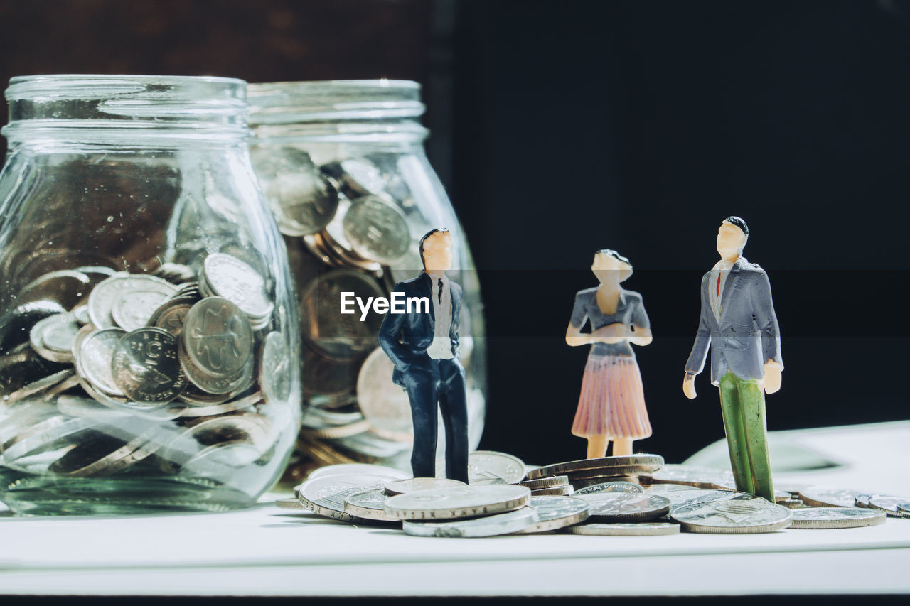 Close-up of figurine by stack coins in glass on table