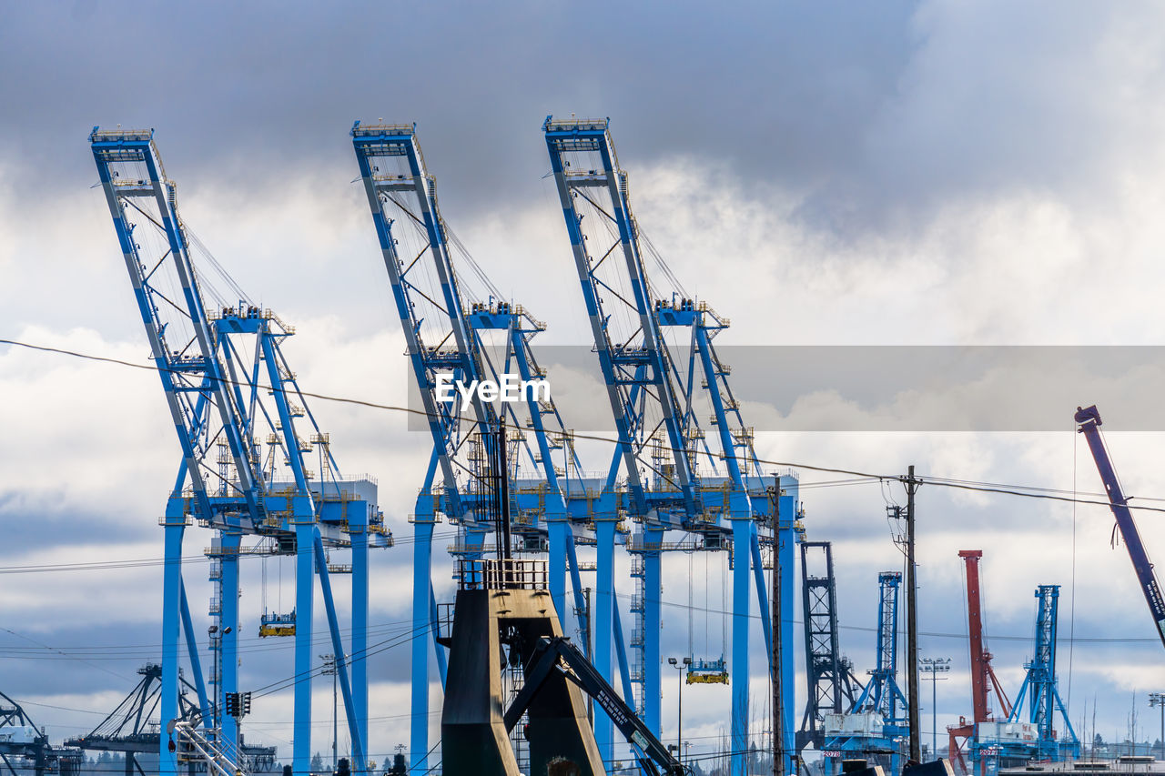 Large blue cranes at the port of tacoma with clouds behind.