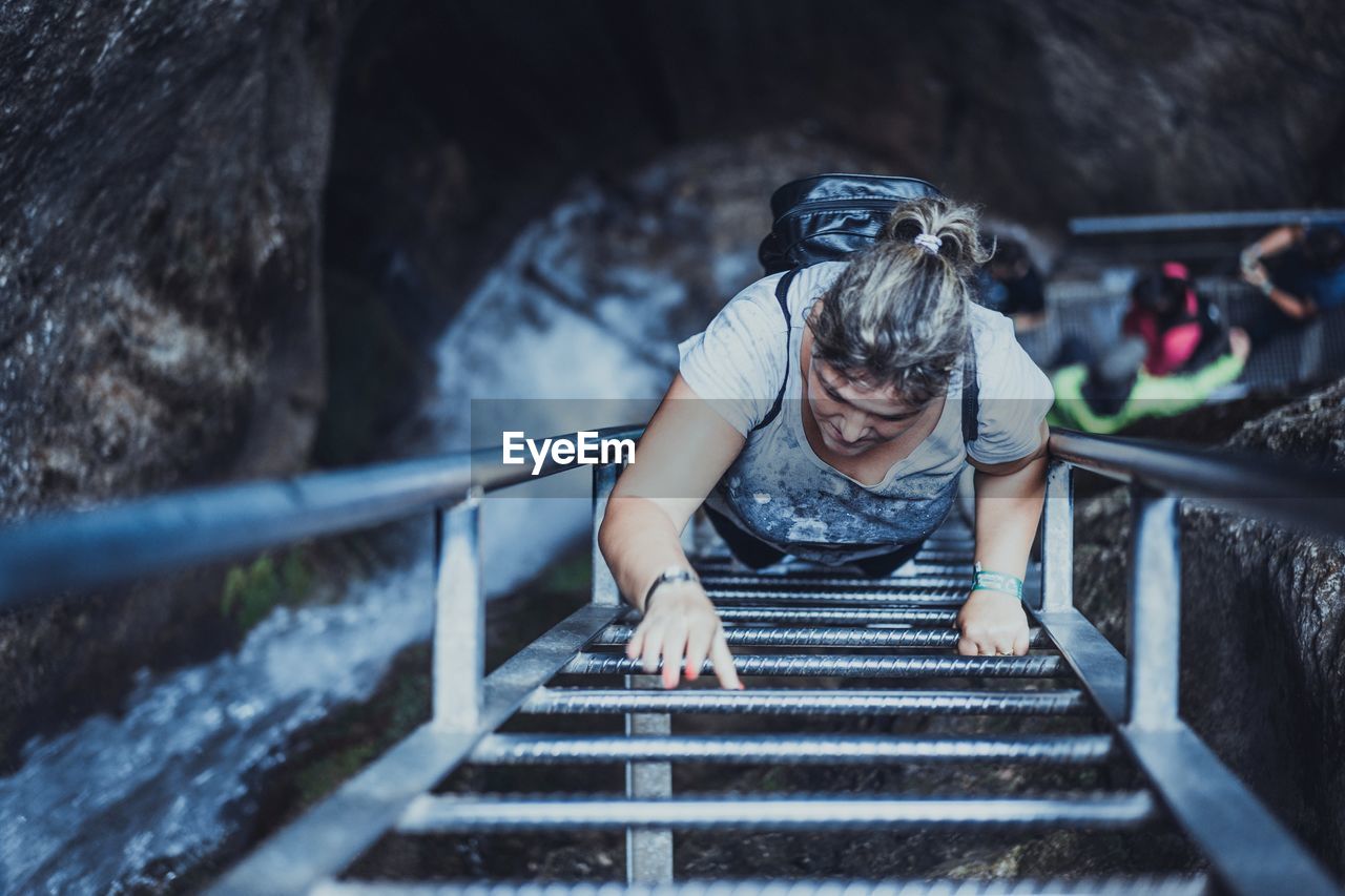 High angle view of mid adult woman moving up on ladder