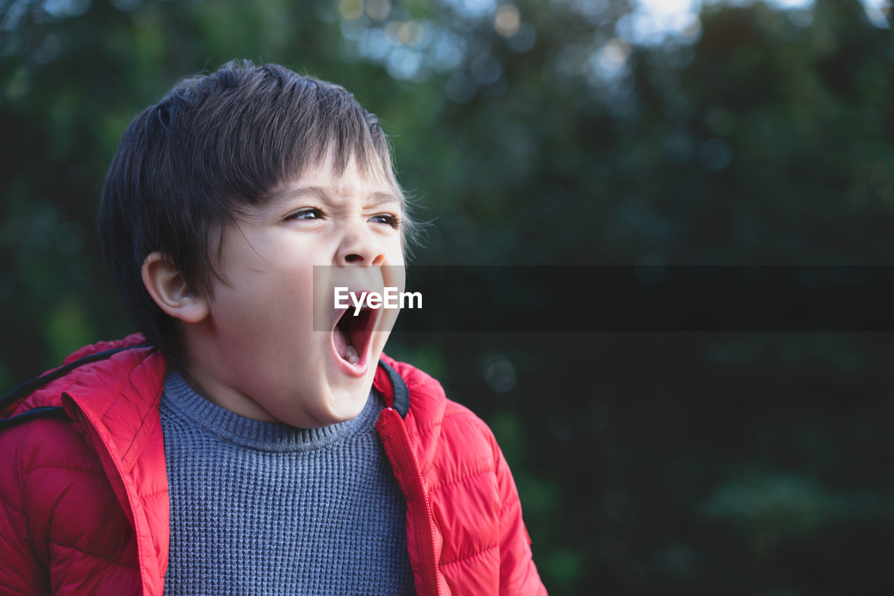 Cute boy yawning while standing outdoors
