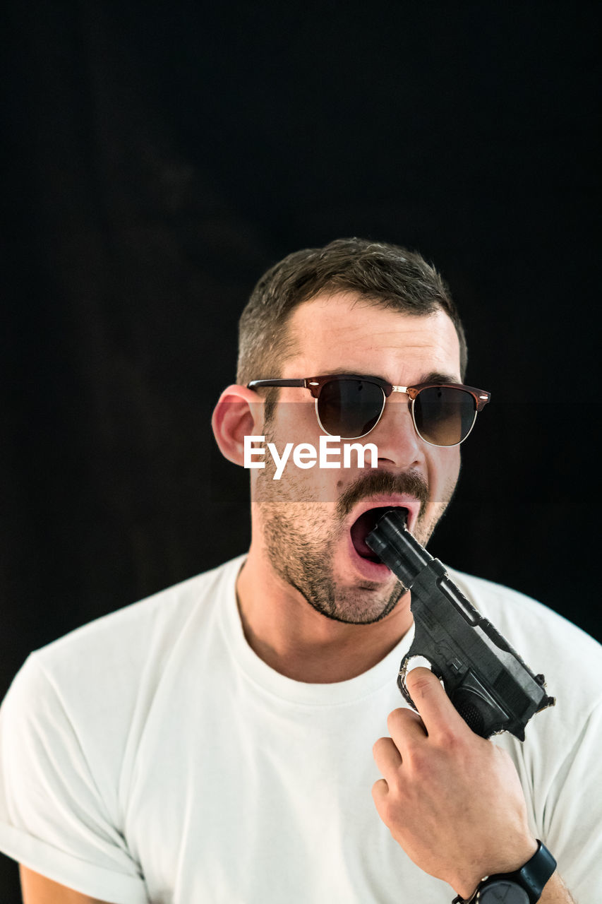 Man pointing gun in mouth against black background