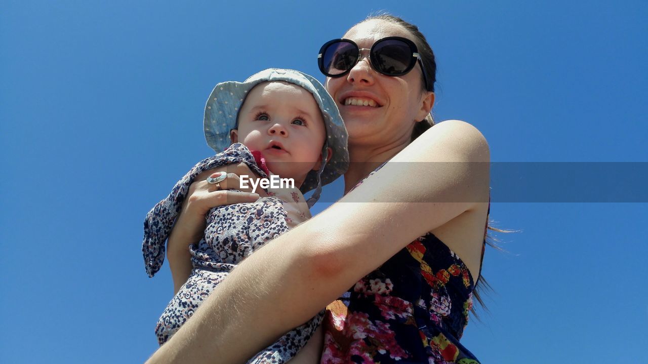 Low angle view of happy mother holding daughter against clear blue sky