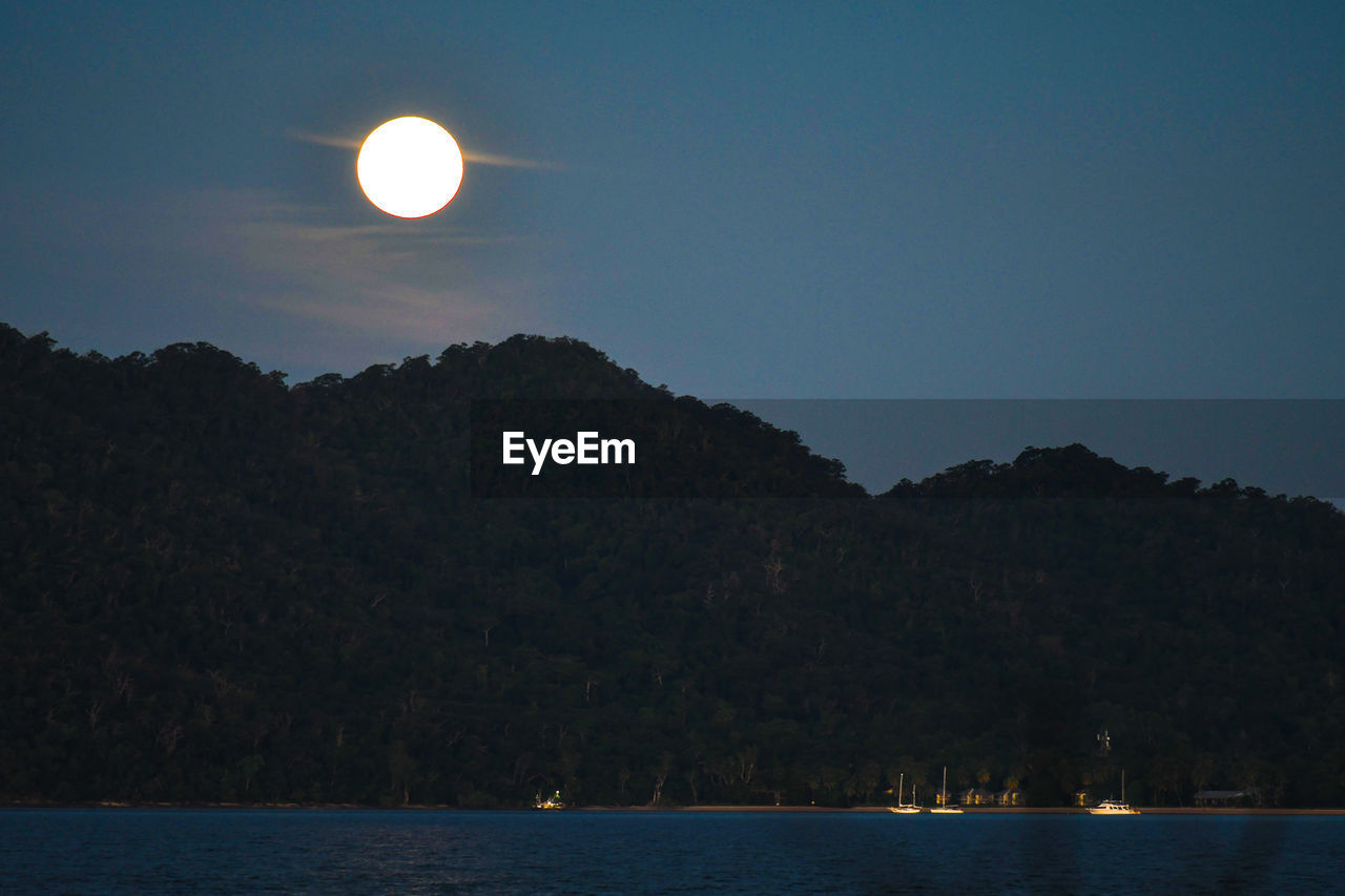 SCENIC VIEW OF SEA AND MOUNTAINS AGAINST CLEAR SKY AT NIGHT