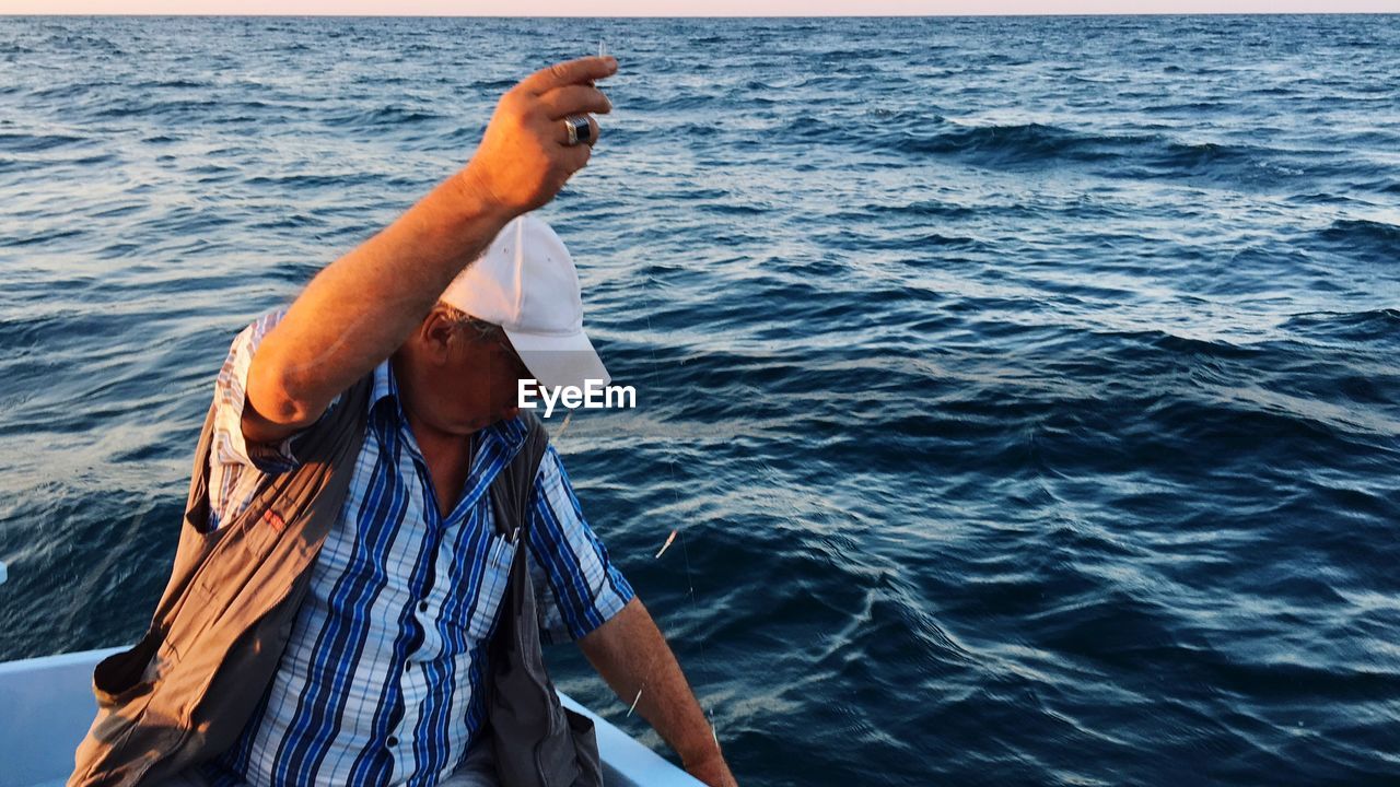 Man sitting on boat while fishing in sea