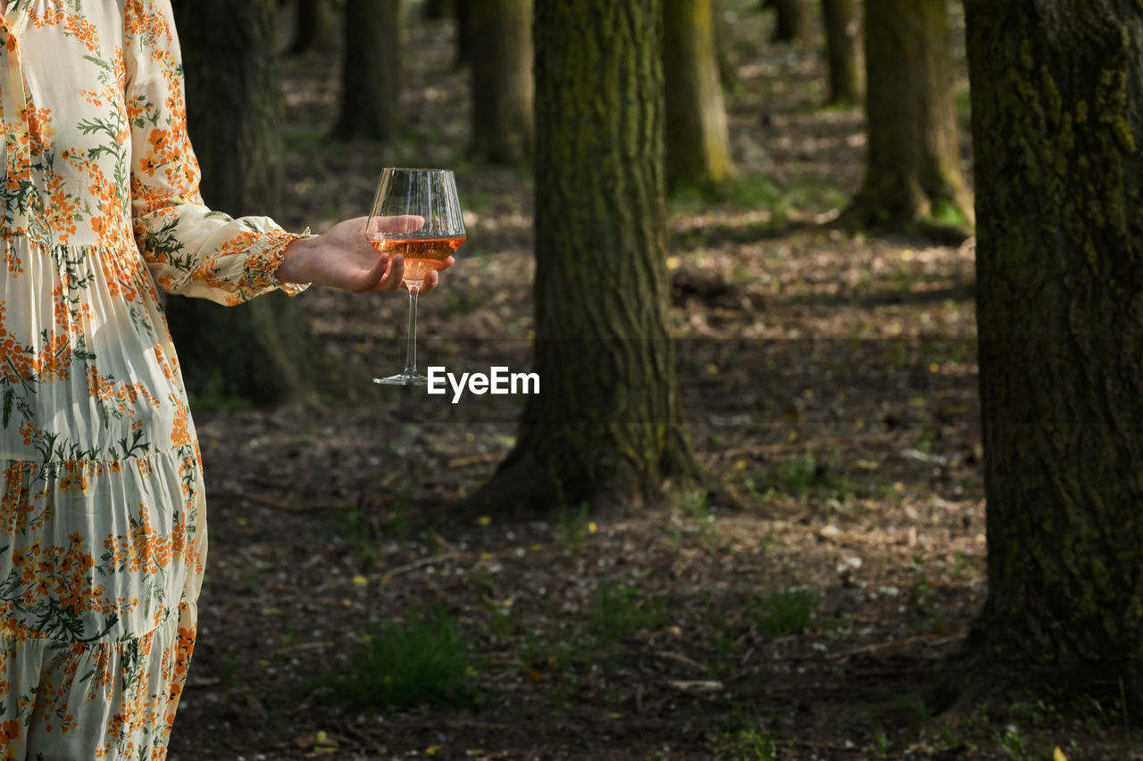 Abstract young woman with glass of rose wine in forest