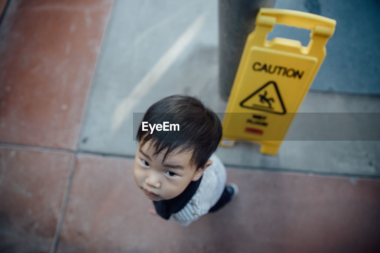 High angle view of boy looking up by warning sign