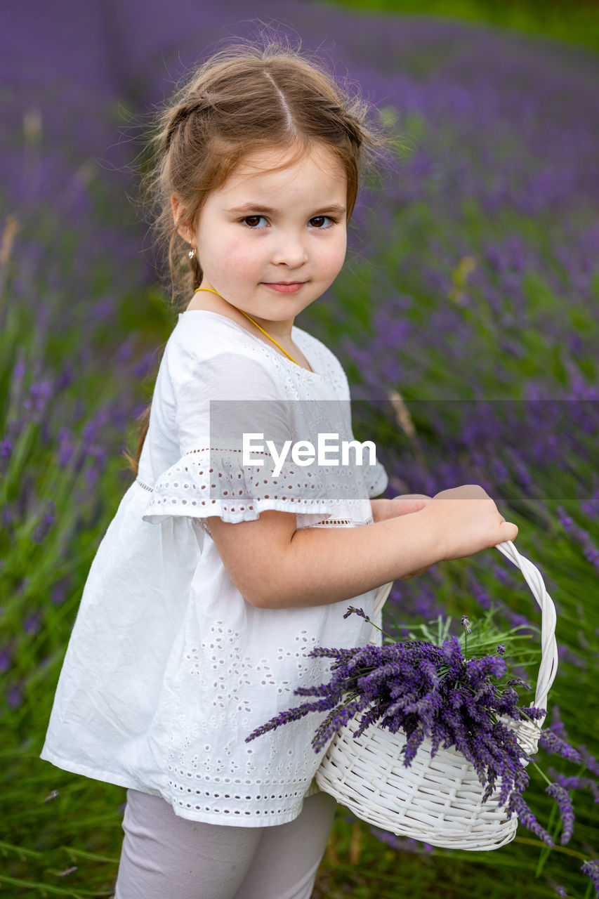 Portrait of cute girl collecting purple flowers on field