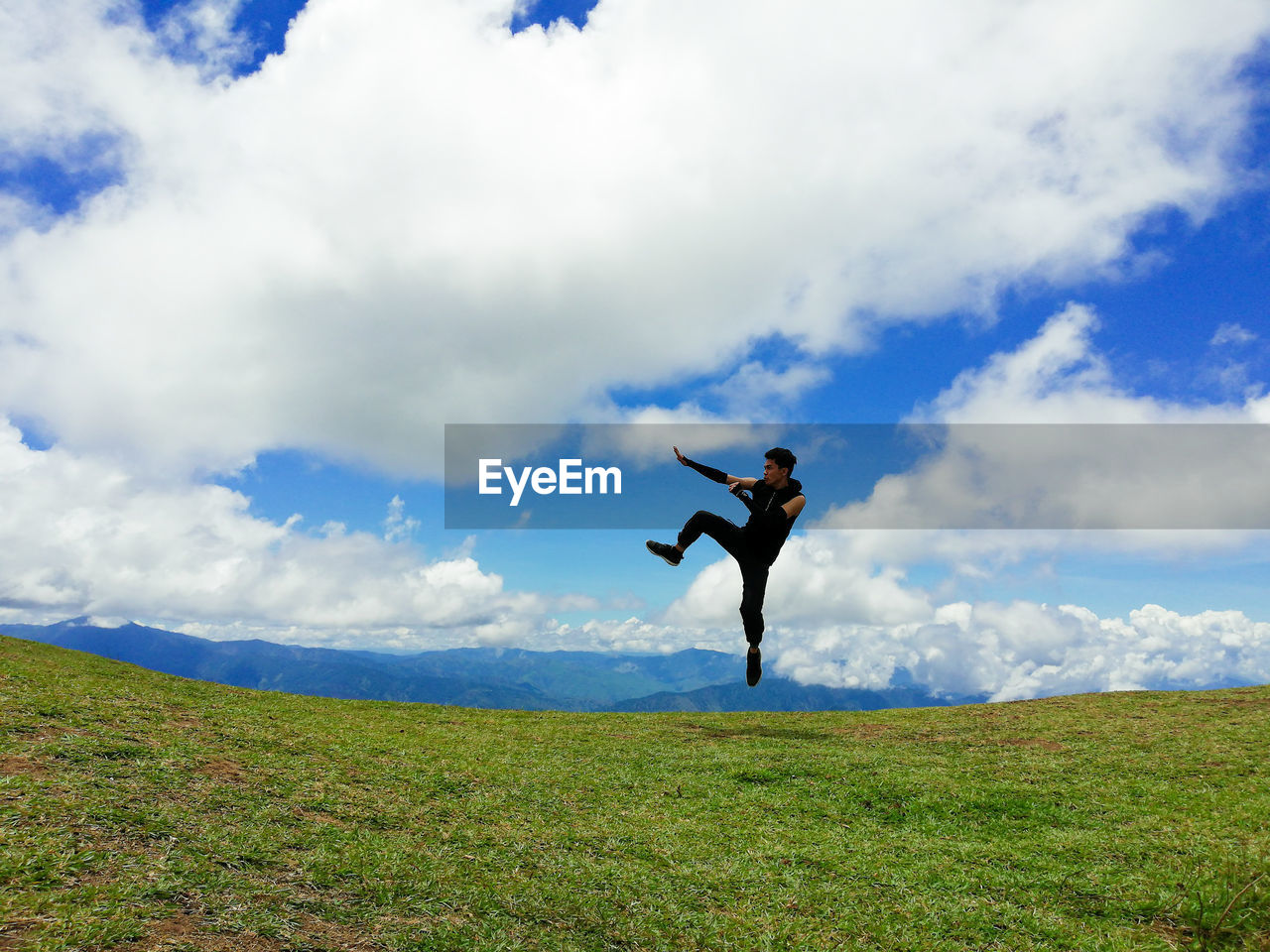 Young man jumping on grassy field against cloudy sky