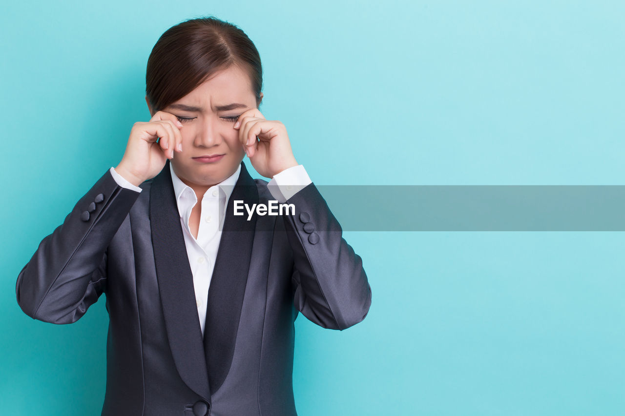 Businesswoman crying while standing against blue background
