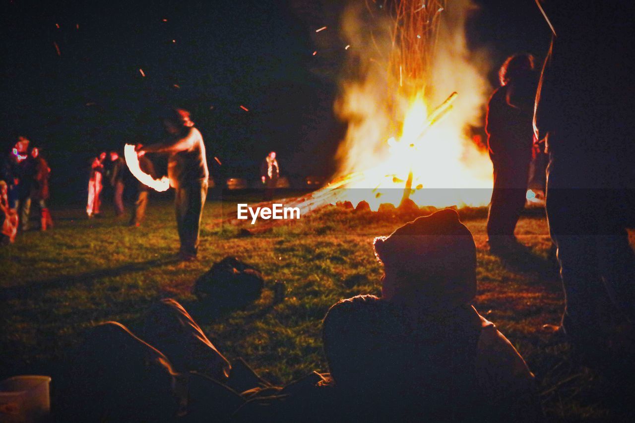 People by lit bonfire against clear sky at night