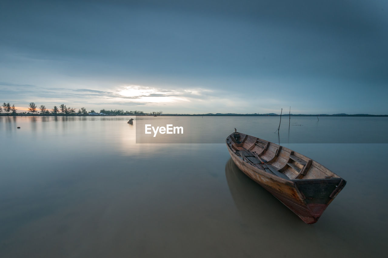 Sailboats moored in lake against sky during sunrise