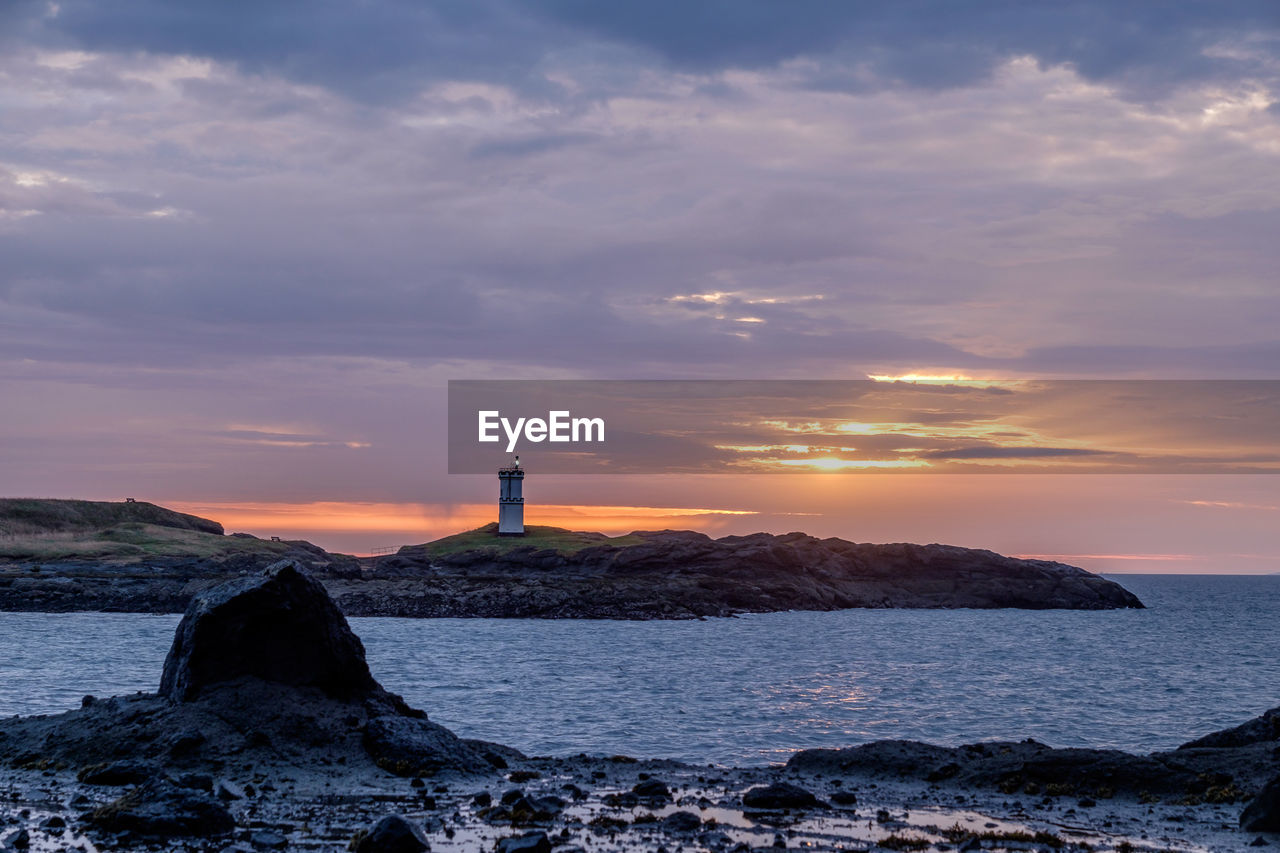 Lighthouse by sea against sky during sunset