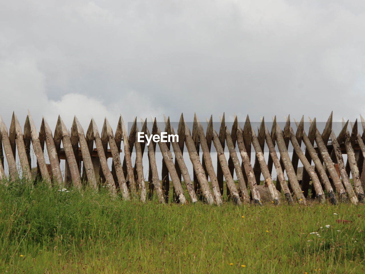 Sharp wooden fence on field against cloudy sky