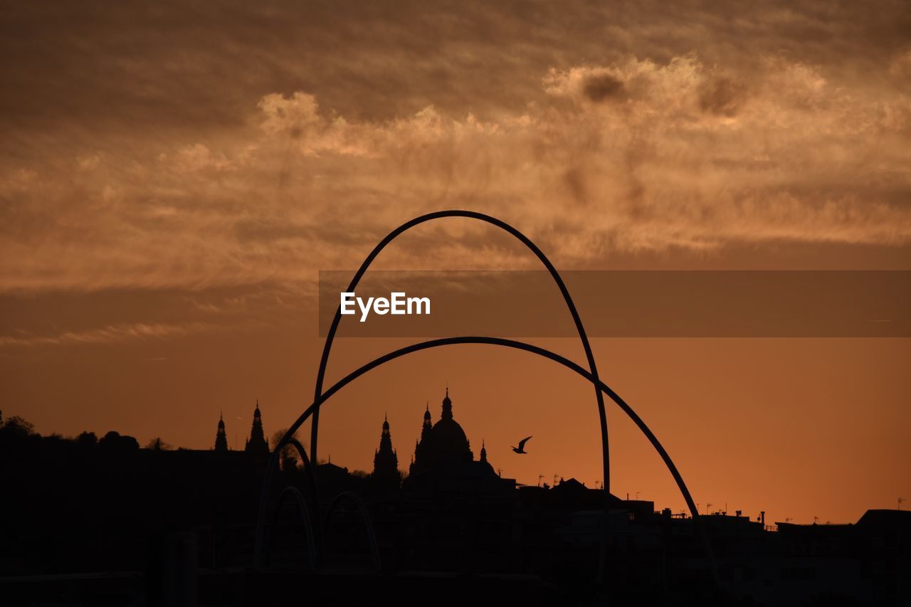 Low angle view of silhouette dome and arches against orange sky