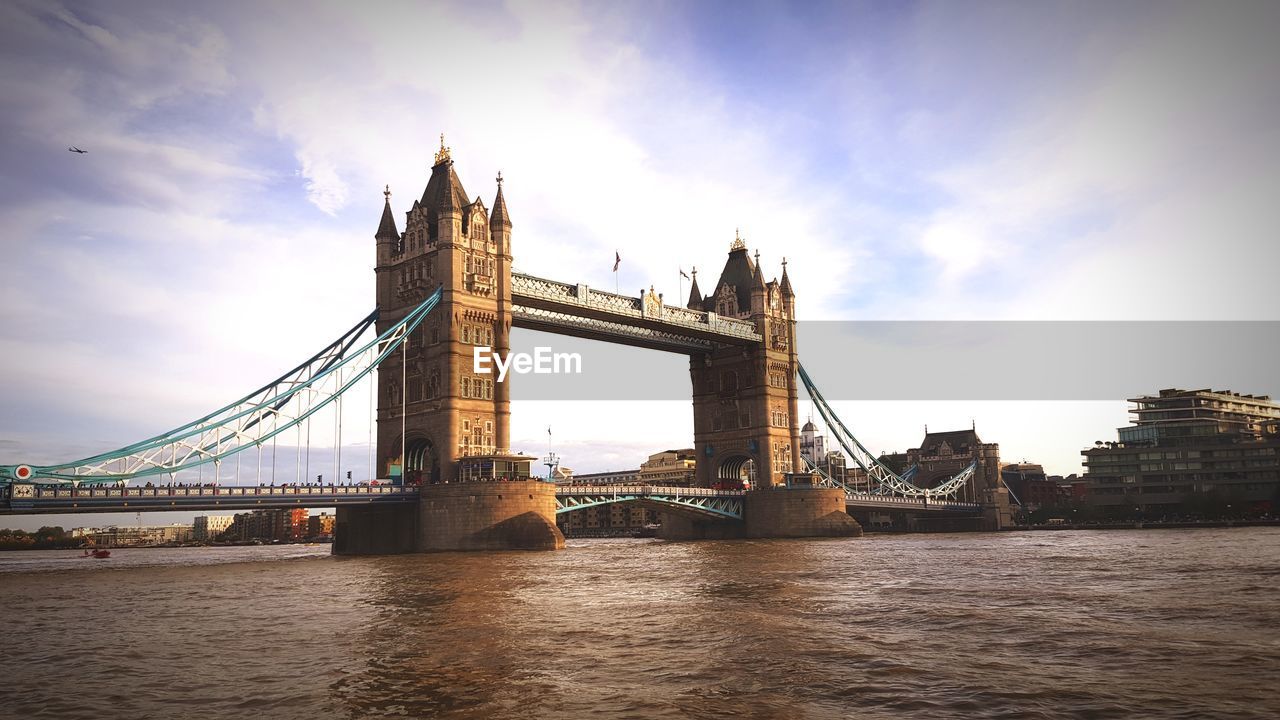 Bridge over thames river against cloudy sky