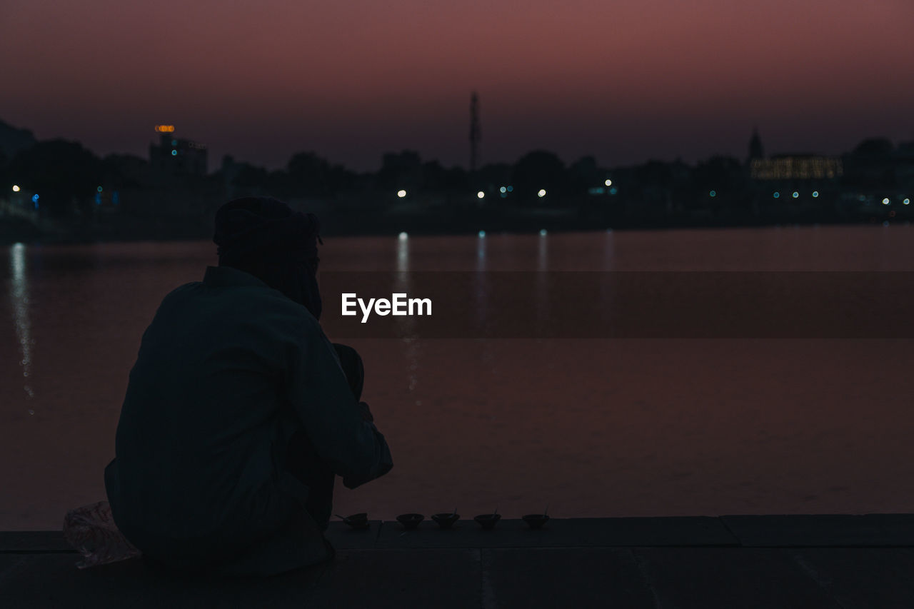 REAR VIEW OF WOMAN LOOKING AT RIVER IN CITY AT NIGHT