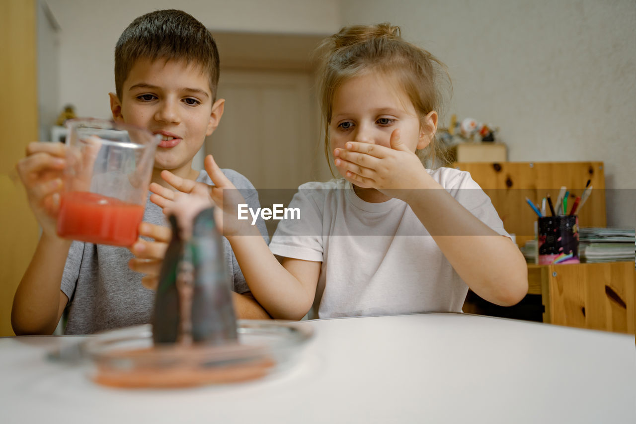 Children, boy and a girl are conducting an experiment with a volcanic eruption at home.