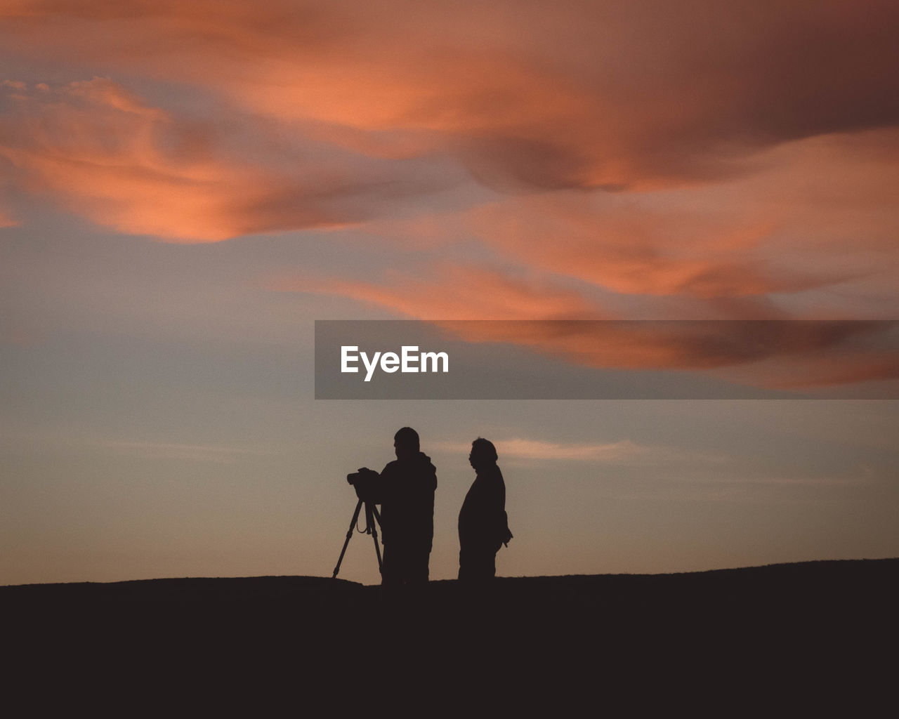 Silhouette people photographing on field during sunset