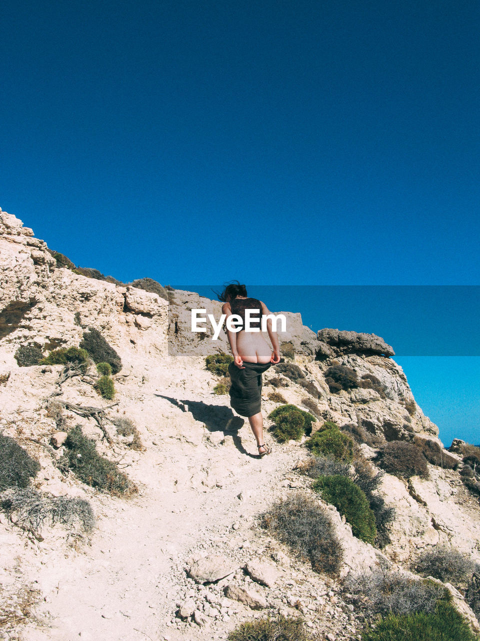 Rear view of woman undressing while walking on mountain against clear blue sky