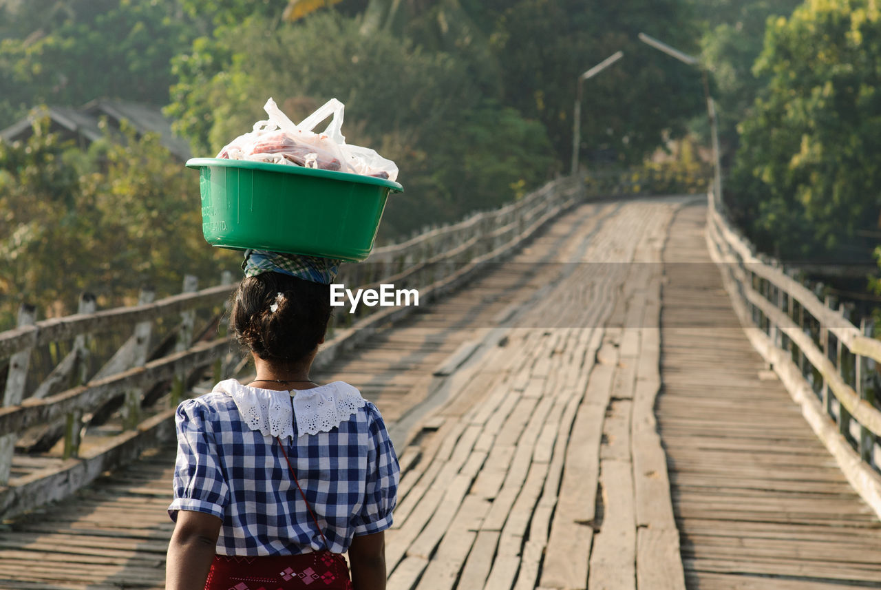 Rear view of woman carrying bucket on footbridge
