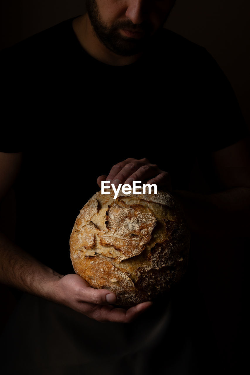 midsection of man holding bread against black background