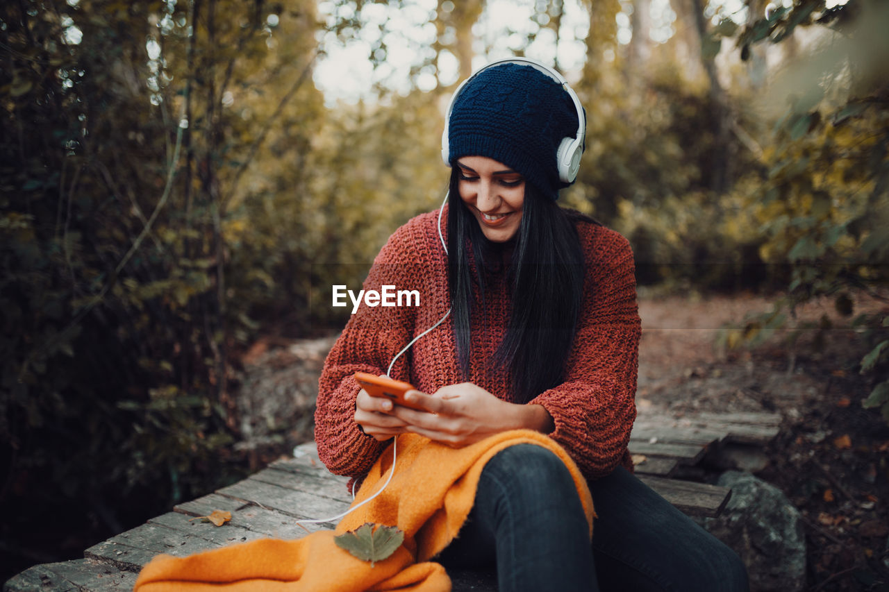 Young woman listening music while using smart phone in forest