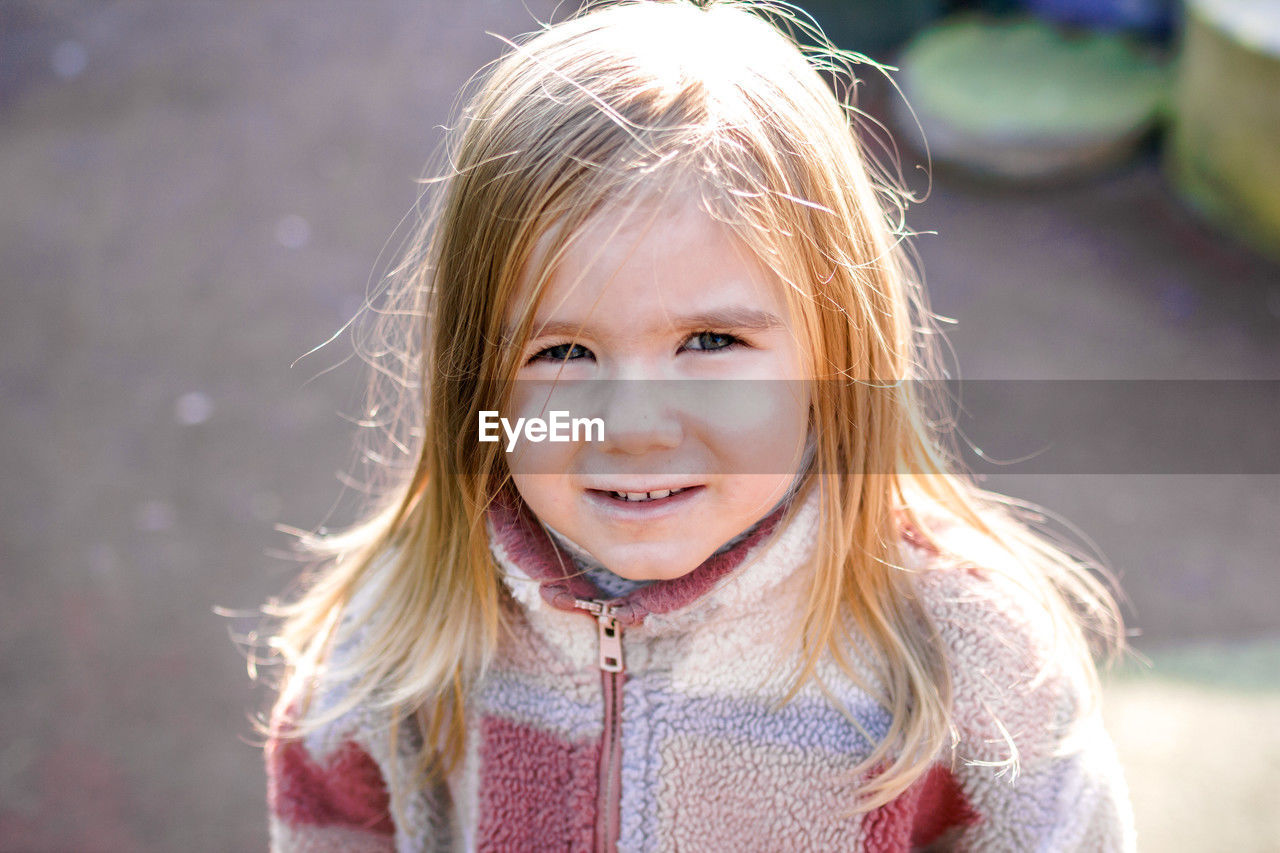 Smiling young girl wearing a stylish checkered jacket a blurred outdoor background of trees.