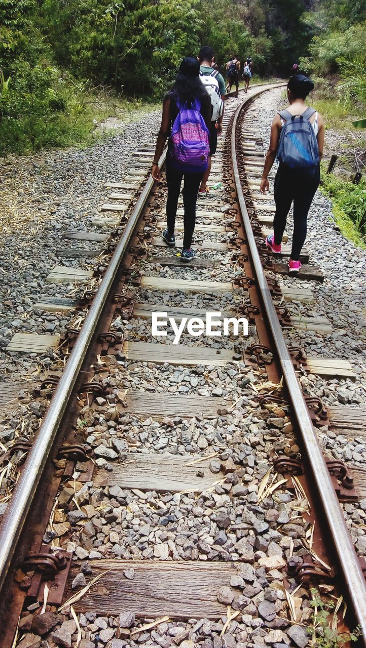 REAR VIEW OF MEN WALKING ON RAILWAY TRACK