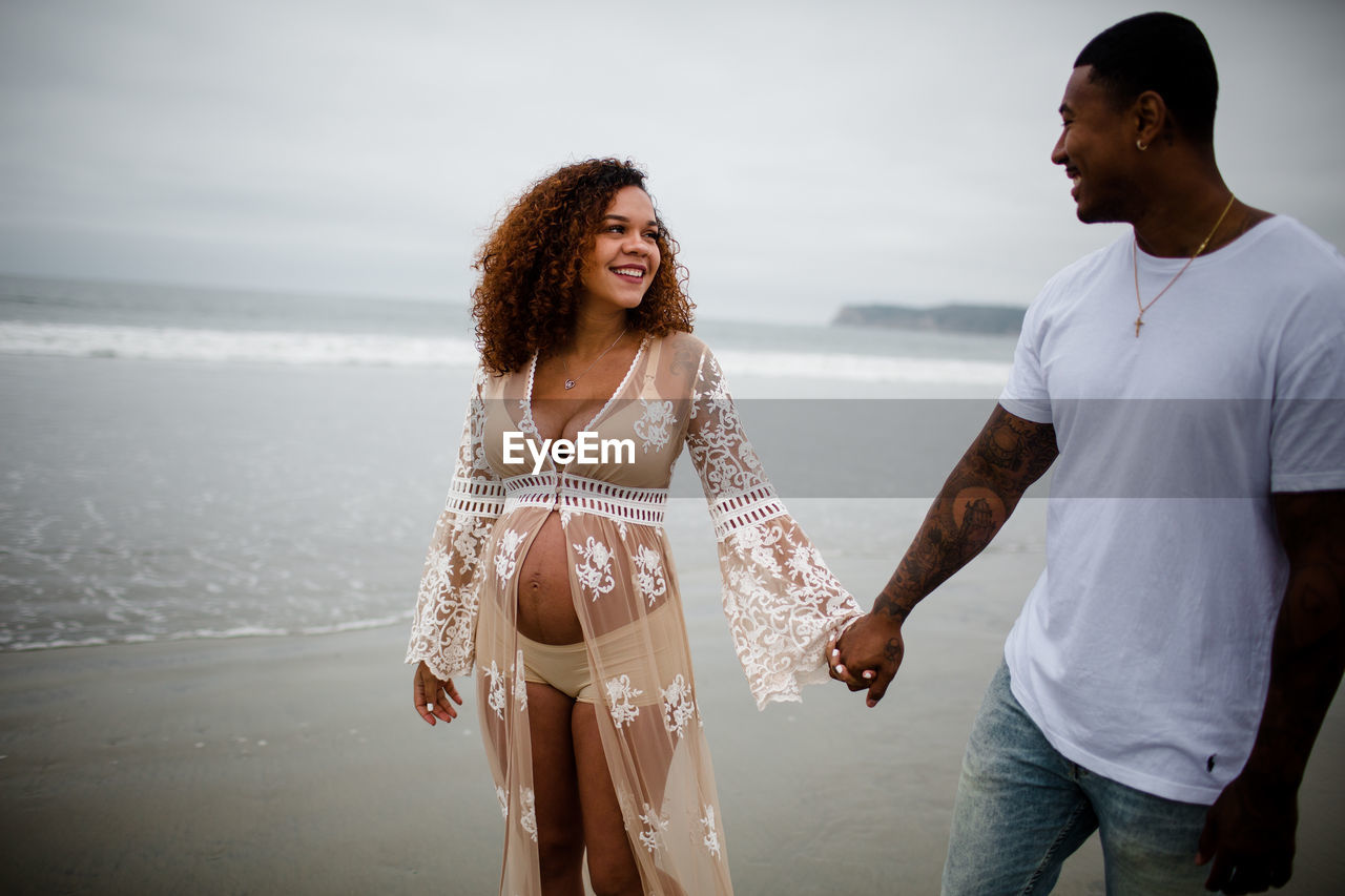 Mixed race couple smiling & walking on beach