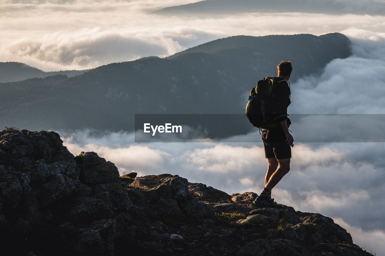 Male hiker on summit gazes at mountain rising above clouds, maine