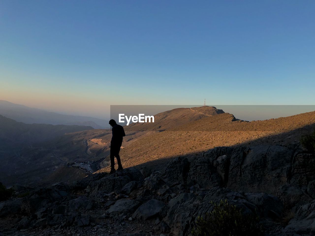 Silhouette man standing on mountain against clear blue sky