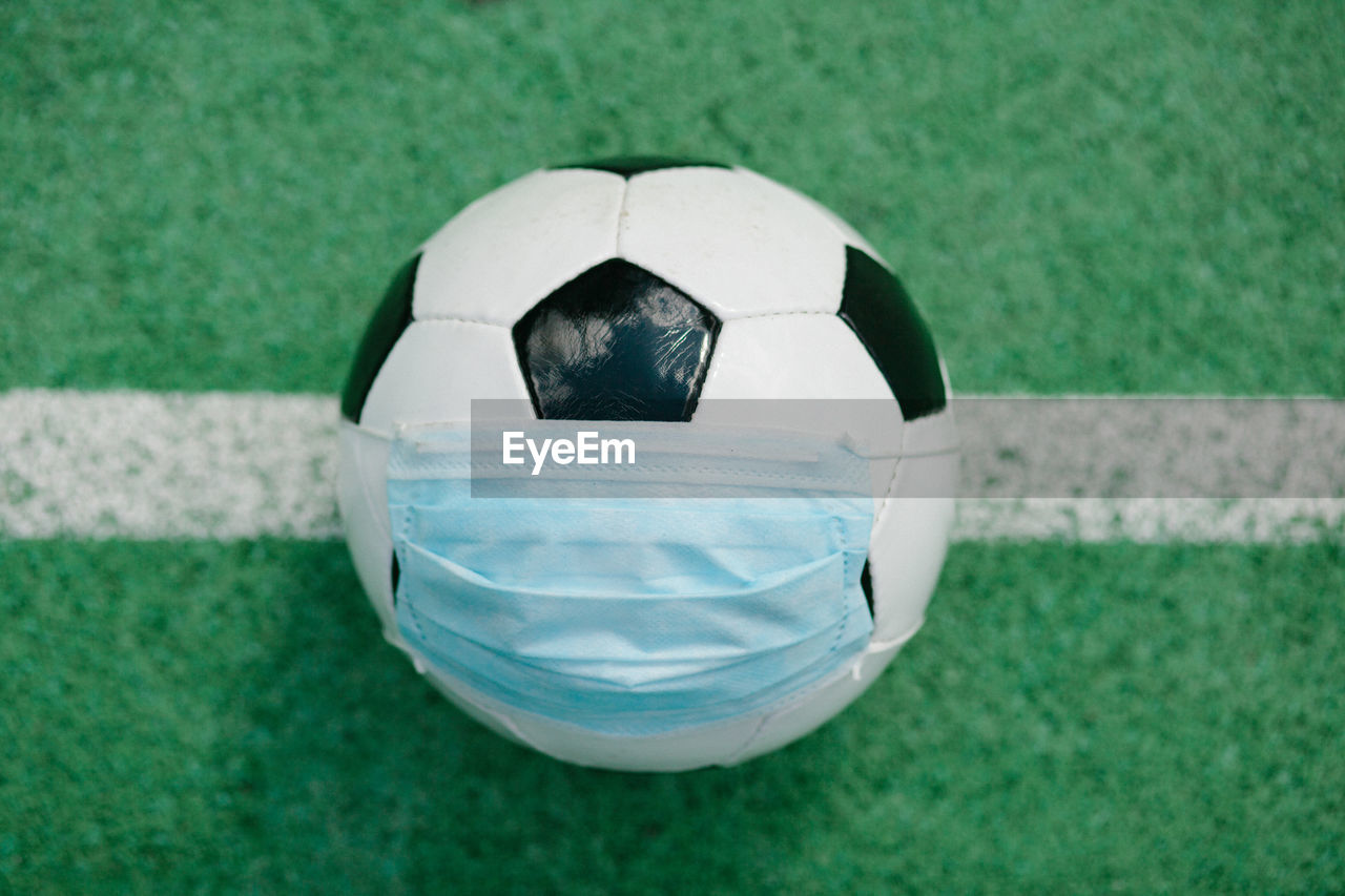 Soccer football with surgical face mask on  turf, symbol for sports during corona covid-19 pandemic
