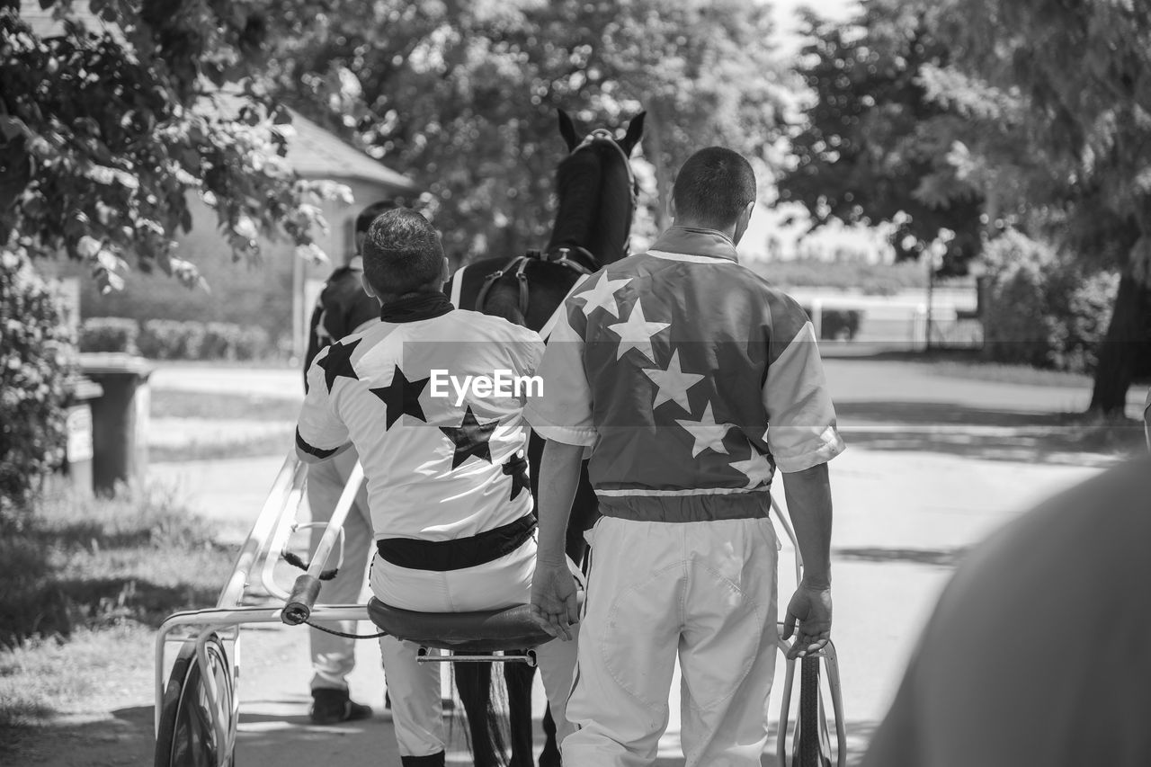 Rear view of jockeys and horse on road during sunny day