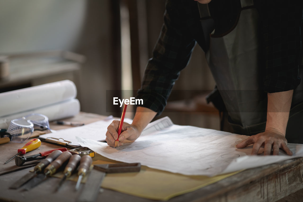 MIDSECTION OF MAN WORKING ON TABLE WITH PAPER