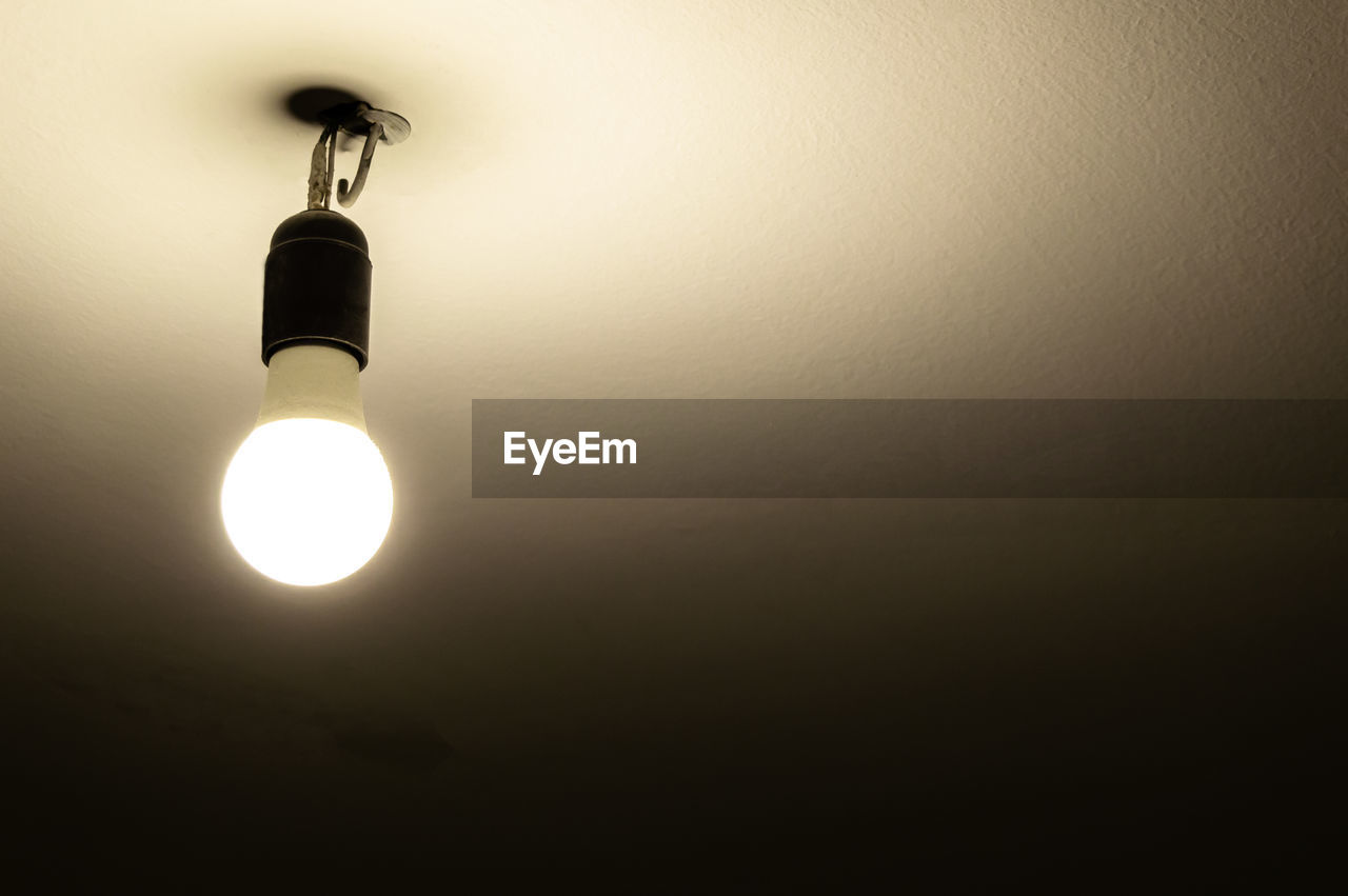 LOW ANGLE VIEW OF ILLUMINATED LIGHT BULB HANGING ON WALL