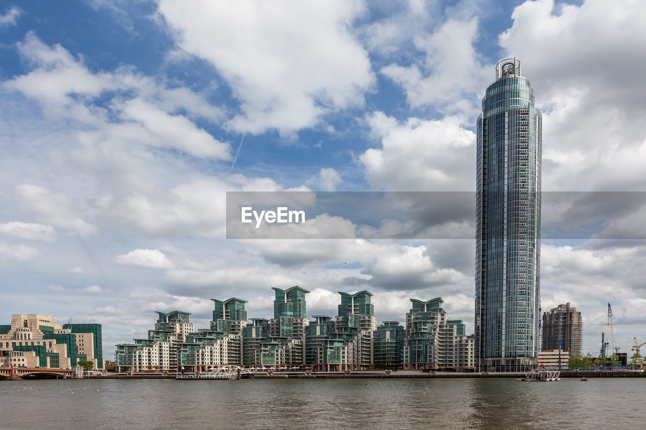 Skyscrapers by river against cloudy sky