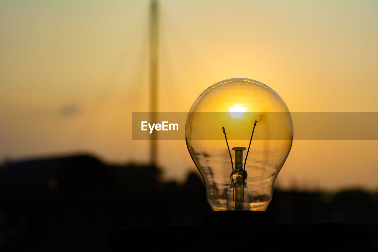 Close-up of light bulb against silhouette landscape during sunset