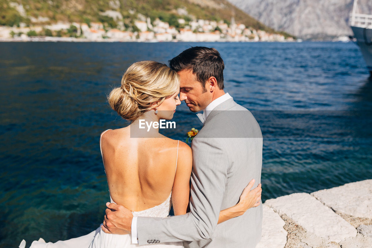 Rear view of couple embracing while sitting against sea