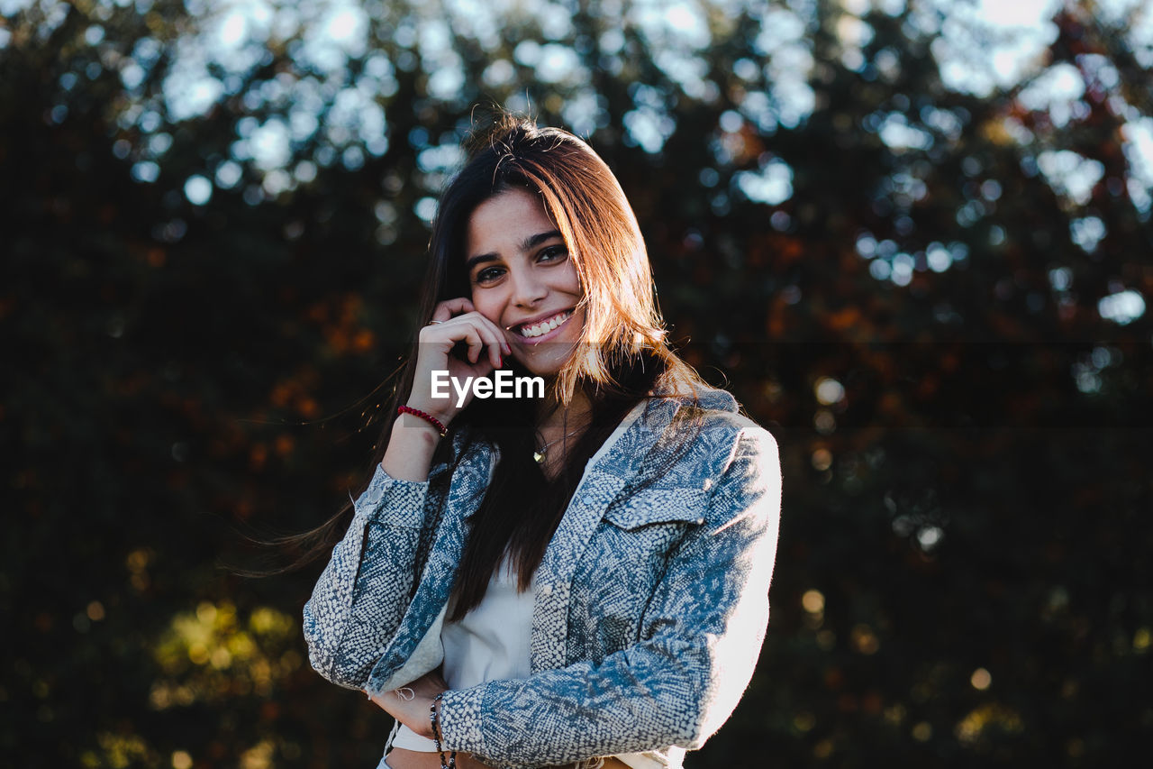 Portrait of smiling teenage girl standing against trees in park