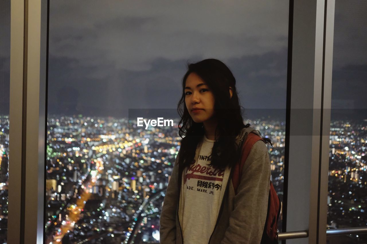 Portrait of beautiful young woman standing by window in city