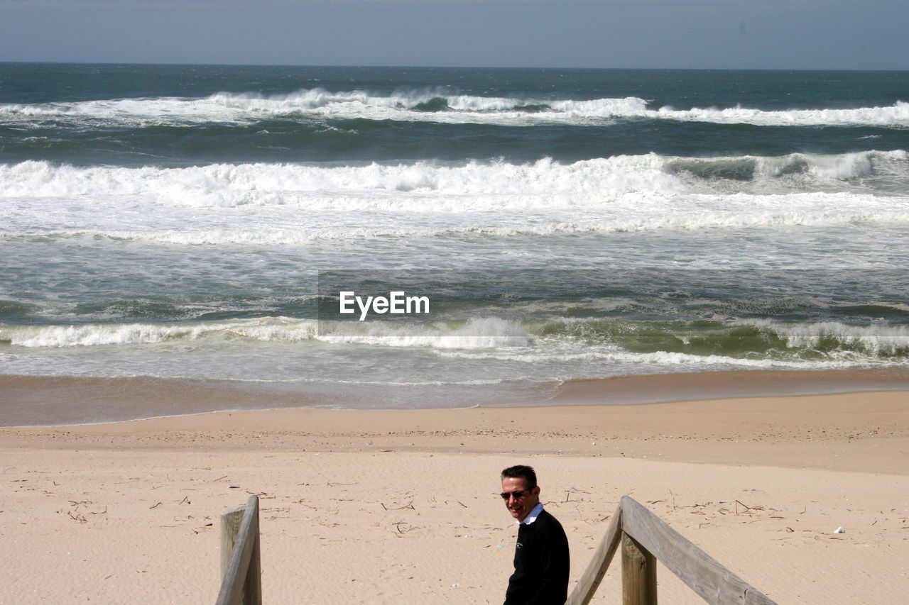 Side view of man wearing sunglasses standing at beach during sunny day