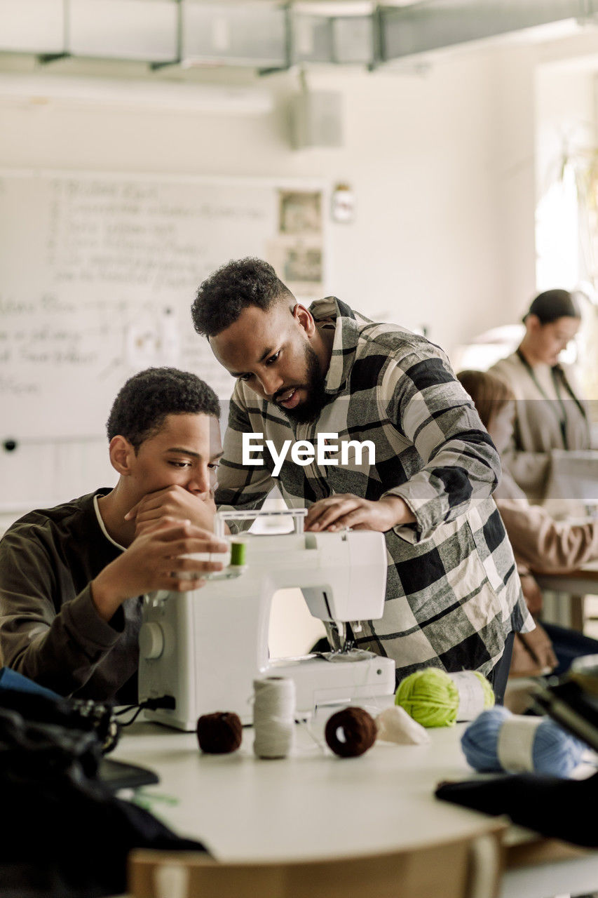 Teacher explaining sewing machine to student in art class at high school