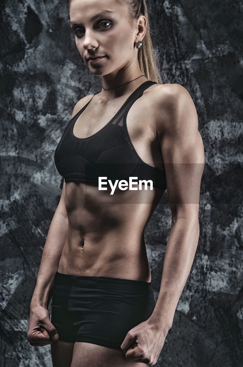 Female athlete in sports clothing standing against wall