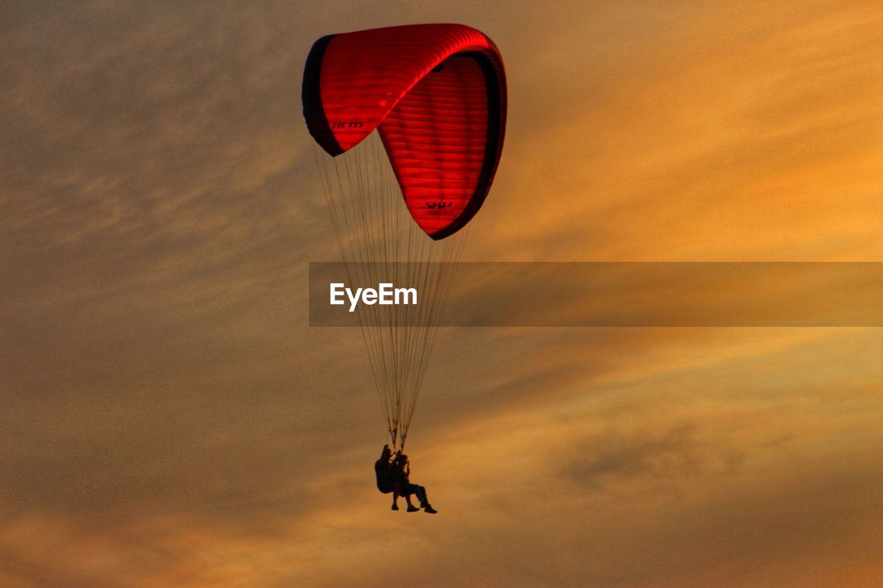 LOW ANGLE VIEW OF PEOPLE PARAGLIDING AGAINST SKY DURING SUNSET