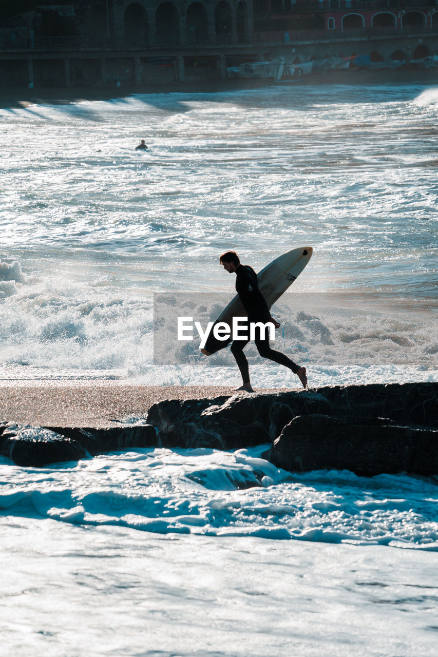 surfing, water, ocean, wave, surfboard, sea, surfing equipment, wind wave, sports, motion, water sports, nature, boardsport, one person, men, leisure activity, full length, extreme sports, day, lifestyles, sports equipment, adventure, outdoors, person, silhouette, beach, beauty in nature, sunlight, adult, land, skill, blue, coast, holiday