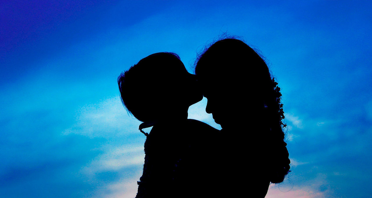 Silhouette daughter kissing mother against blue sky