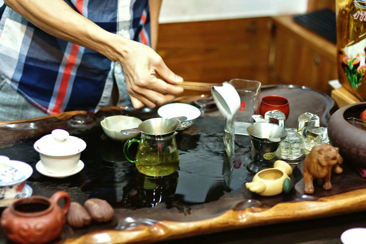 Cropped image of person pouring water in cup on table