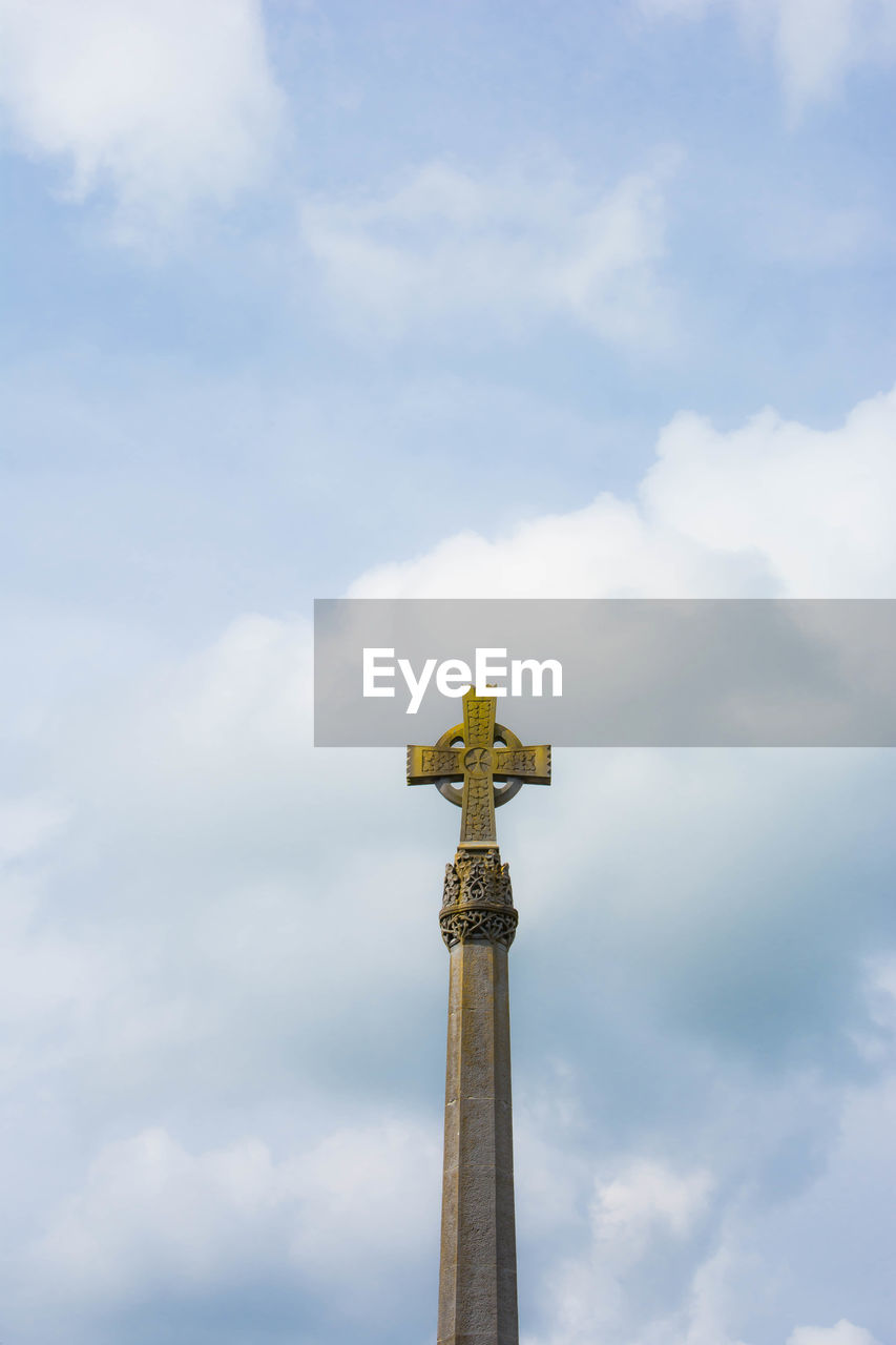 Low angle view of spire with christian cross  against cloudy sky