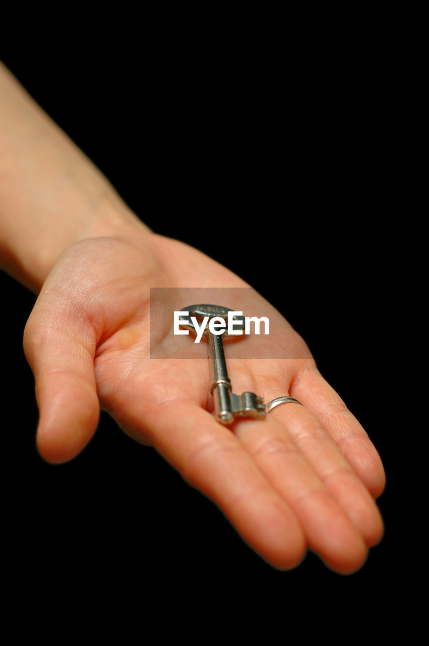 Close-up of hand holding key against black background