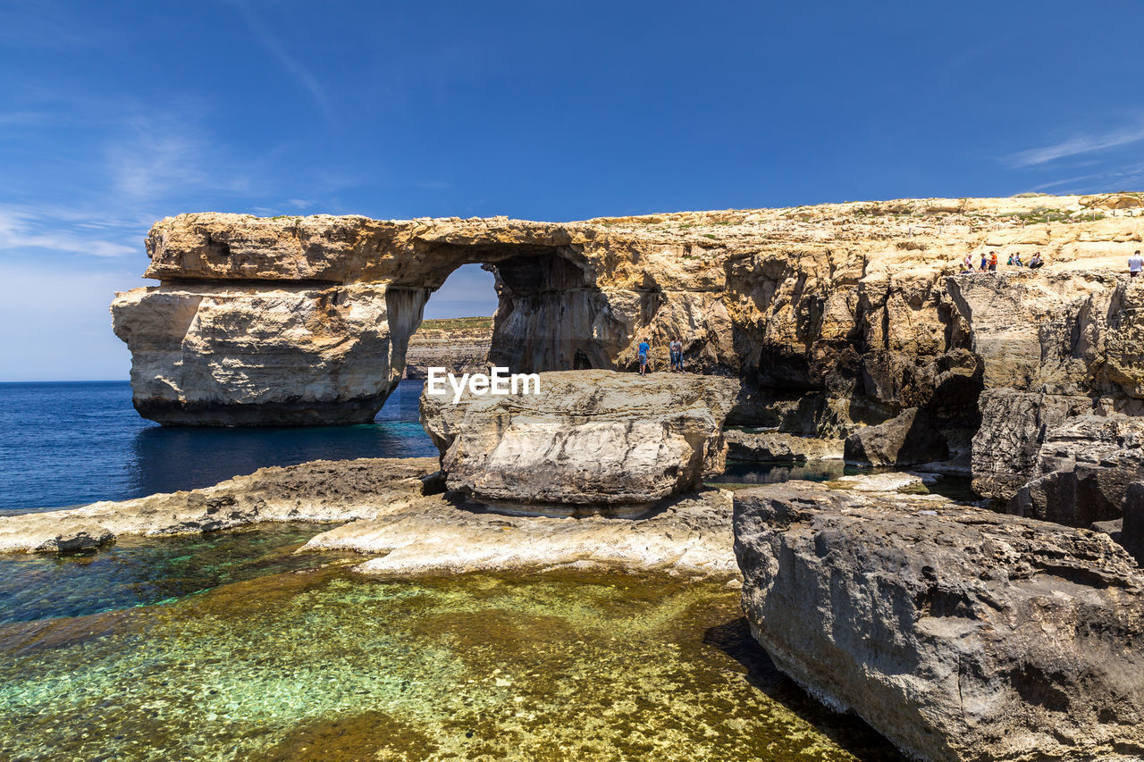 Rocks on cliff by sea against sky